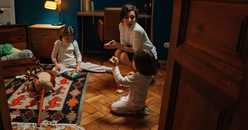 A Woman Sitting on the Floor with Children Playing
