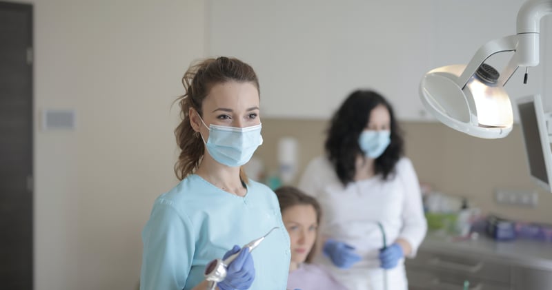 Young female dentist working with assistant while treating patient in modern hospital

