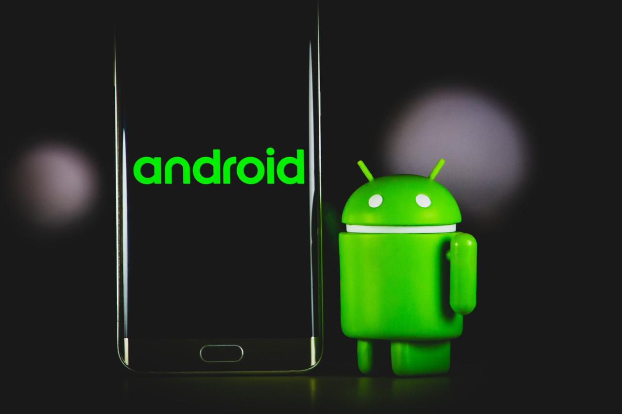 Green Android robot figure beside a smartphone showing the Android wordmark on a black background