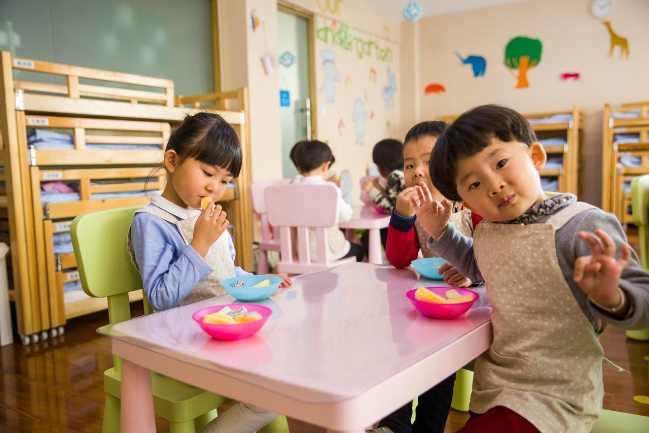 Young children eating snacks at a small pink table, from the daycare teacher salary guide