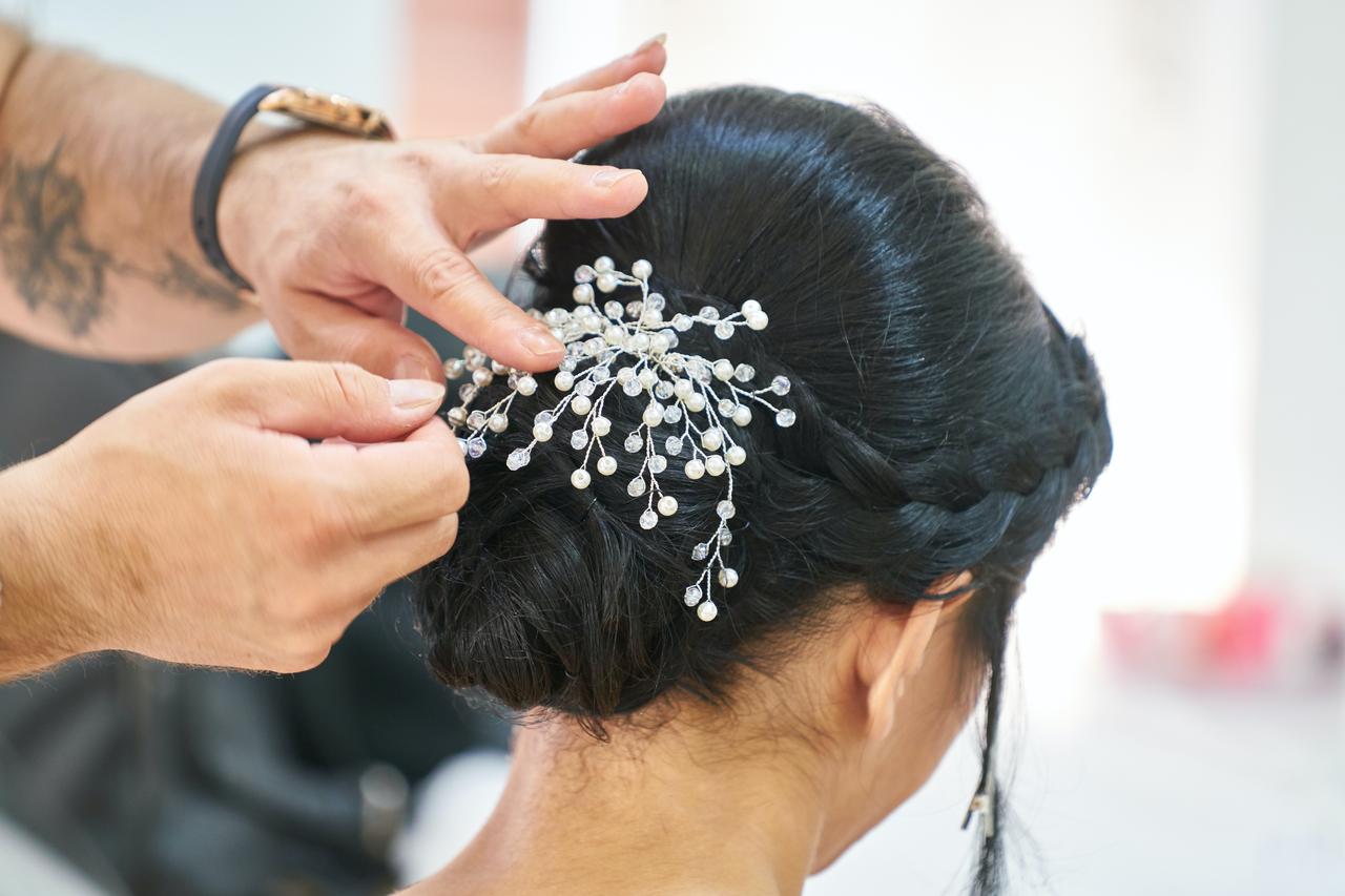 Tattooed hands fixing a crystal and pearl hairpiece into a dark braided updo