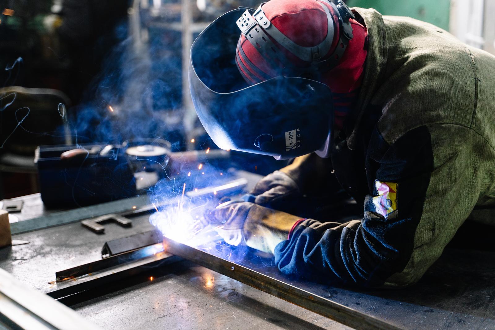 Welder in red helmet welding a steel frame, sparks flying, from the welder career guide
