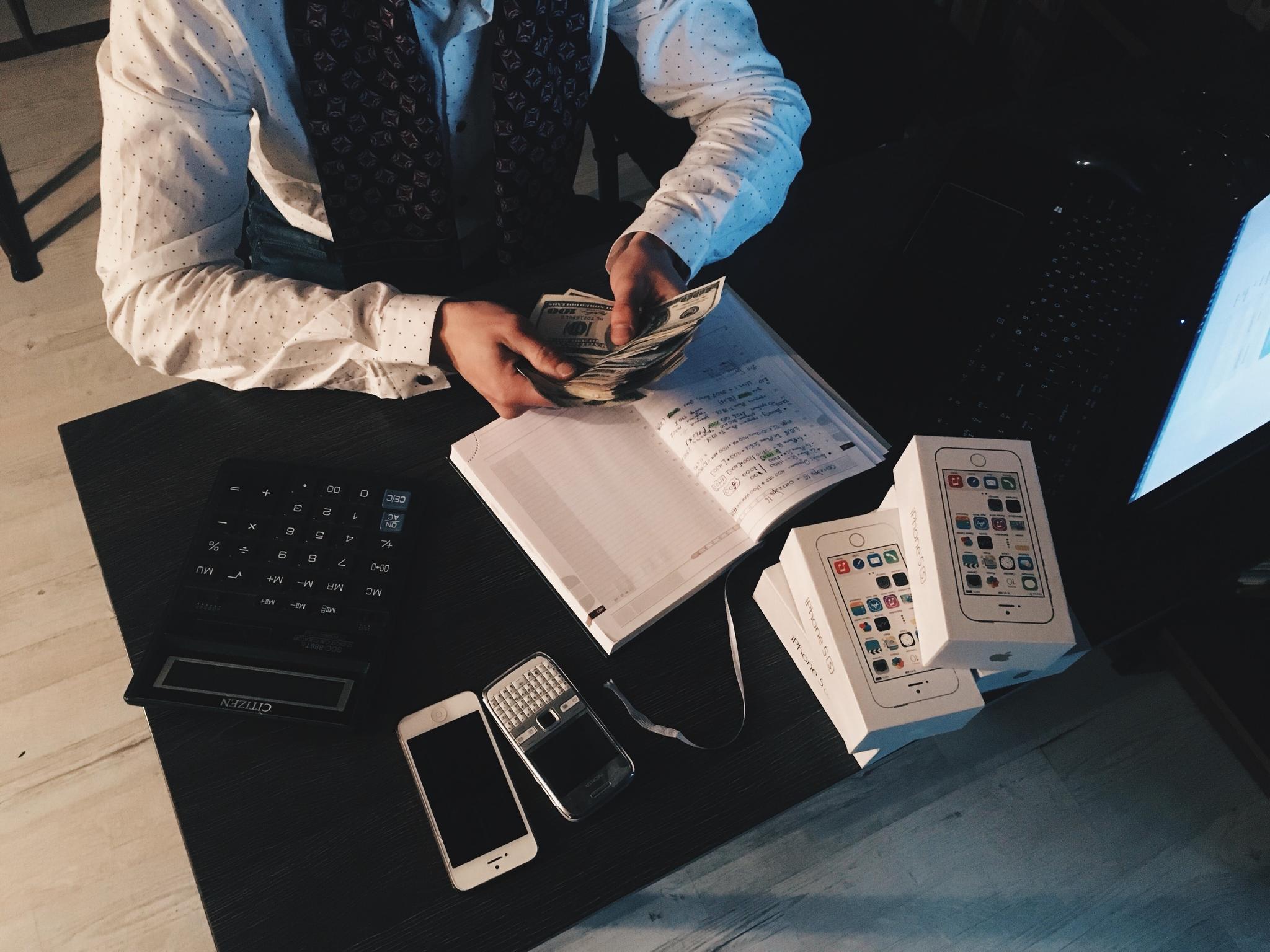 Man counting cash at a desk with notebook and phones, from the bookkeeper career guide