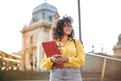 Student in a yellow shirt holding a red folder outside a domed building