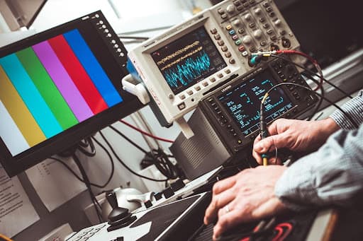 Hands probing oscilloscopes and signal test equipment on an electronics lab bench