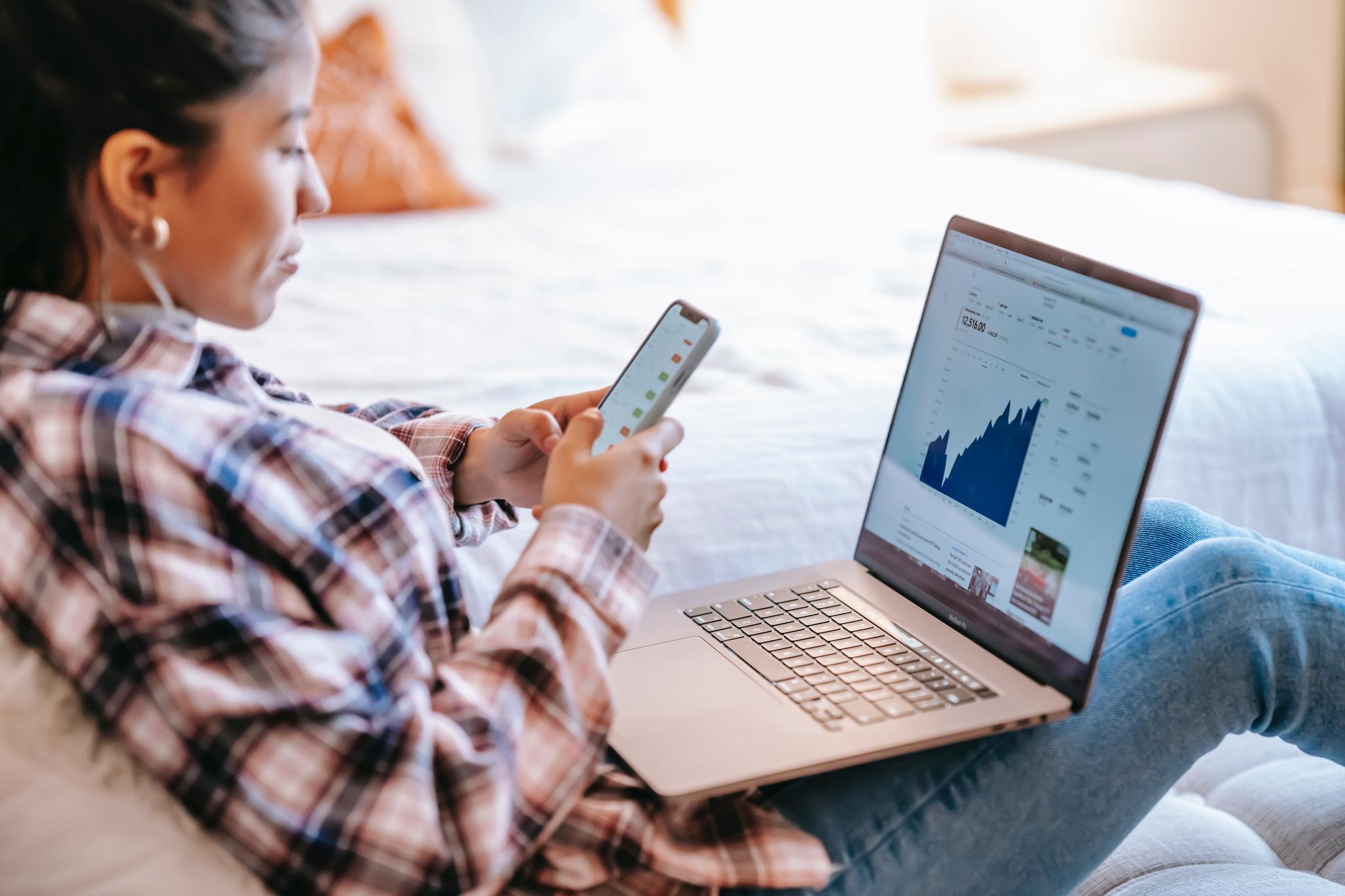 Woman checking her phone beside a laptop showing charts, from the data analyst resume guide