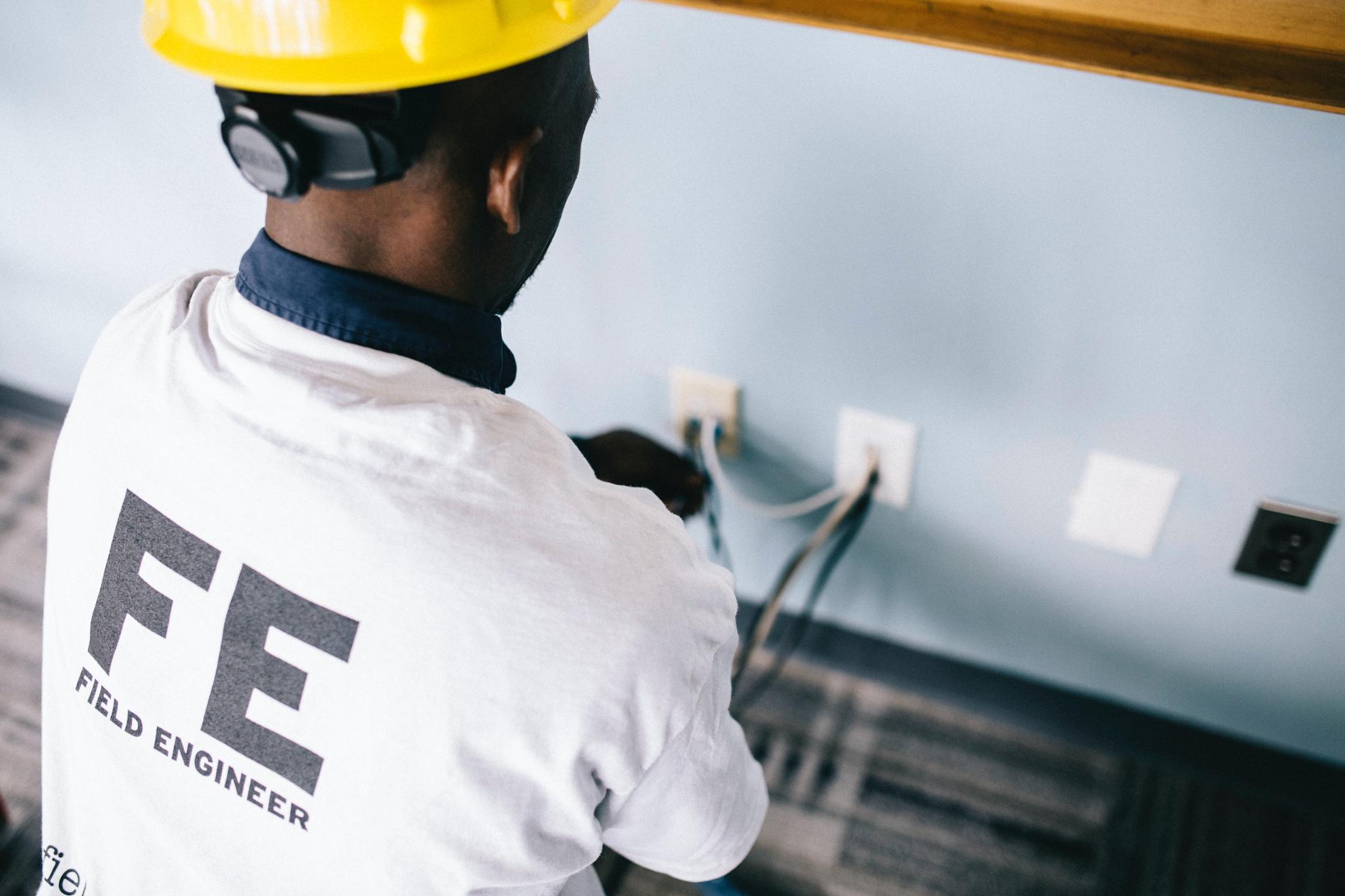 Worker in a yellow hard hat wiring wall outlets, from the electrician career guide