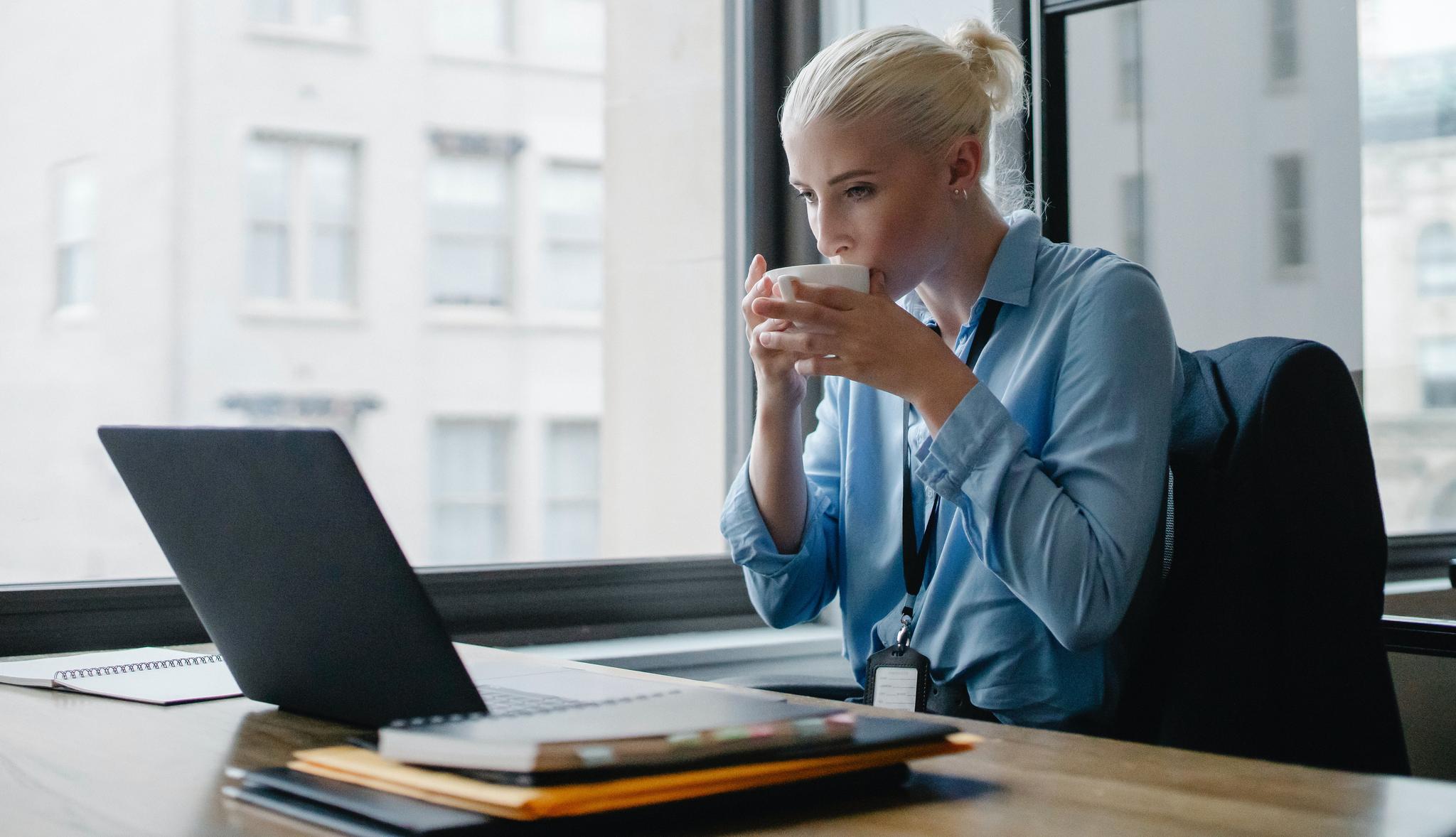 Office professional drinking coffee at her desk, from the executive assistant resume guide