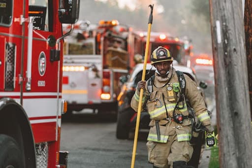 Firefighter in turnout gear carrying a pike pole past parked fire engines