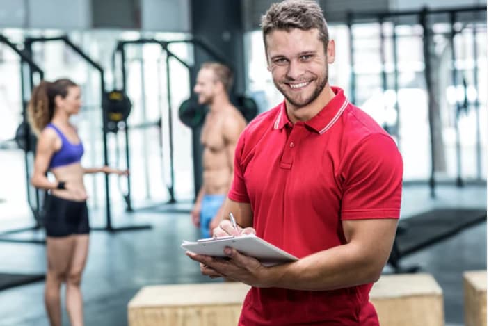 Smiling man in a red polo holds a clipboard and pen inside a gym
