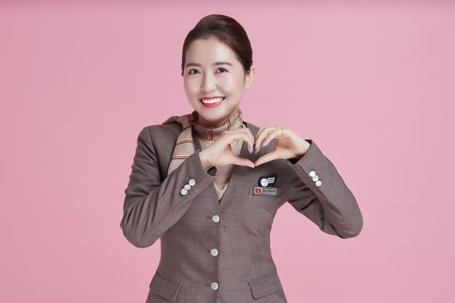 Flight attendant in uniform making a heart shape with her hands against pink backdrop