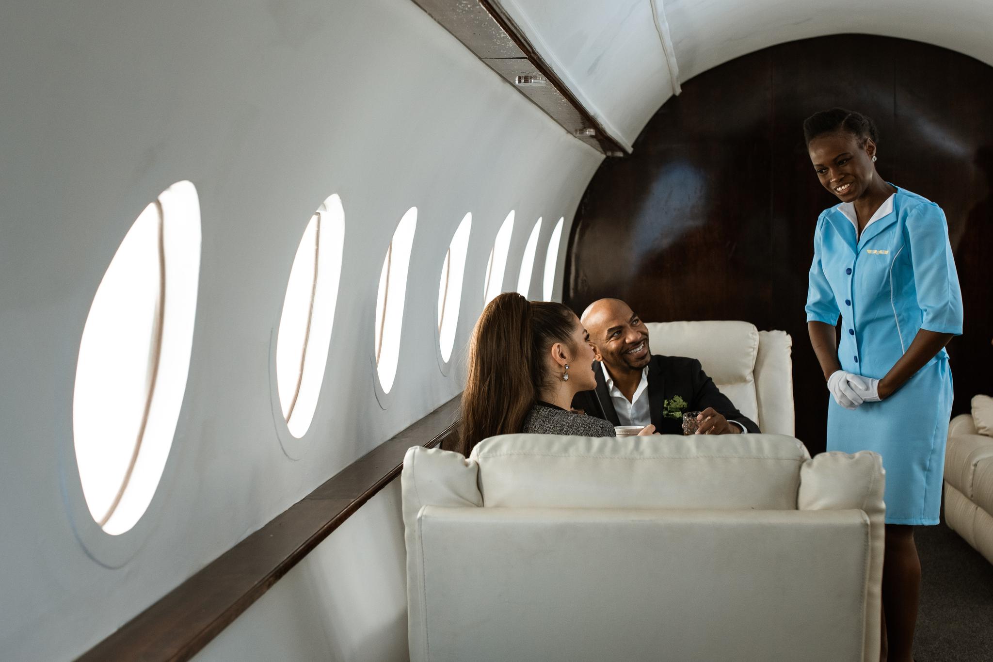 Flight attendant in blue uniform greeting passengers aboard a private jet