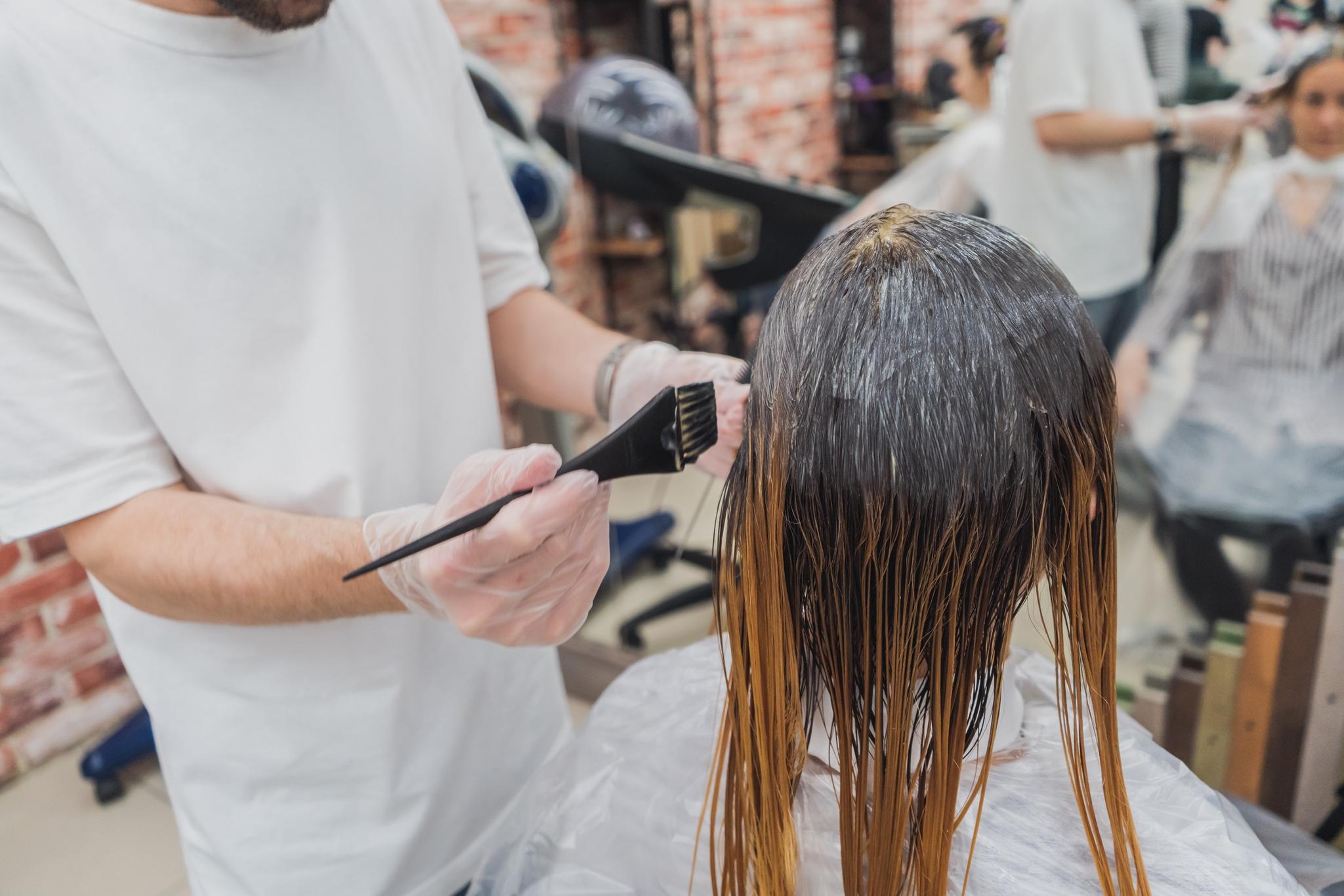 Stylist in a white shirt brushing color onto a client's long wet hair