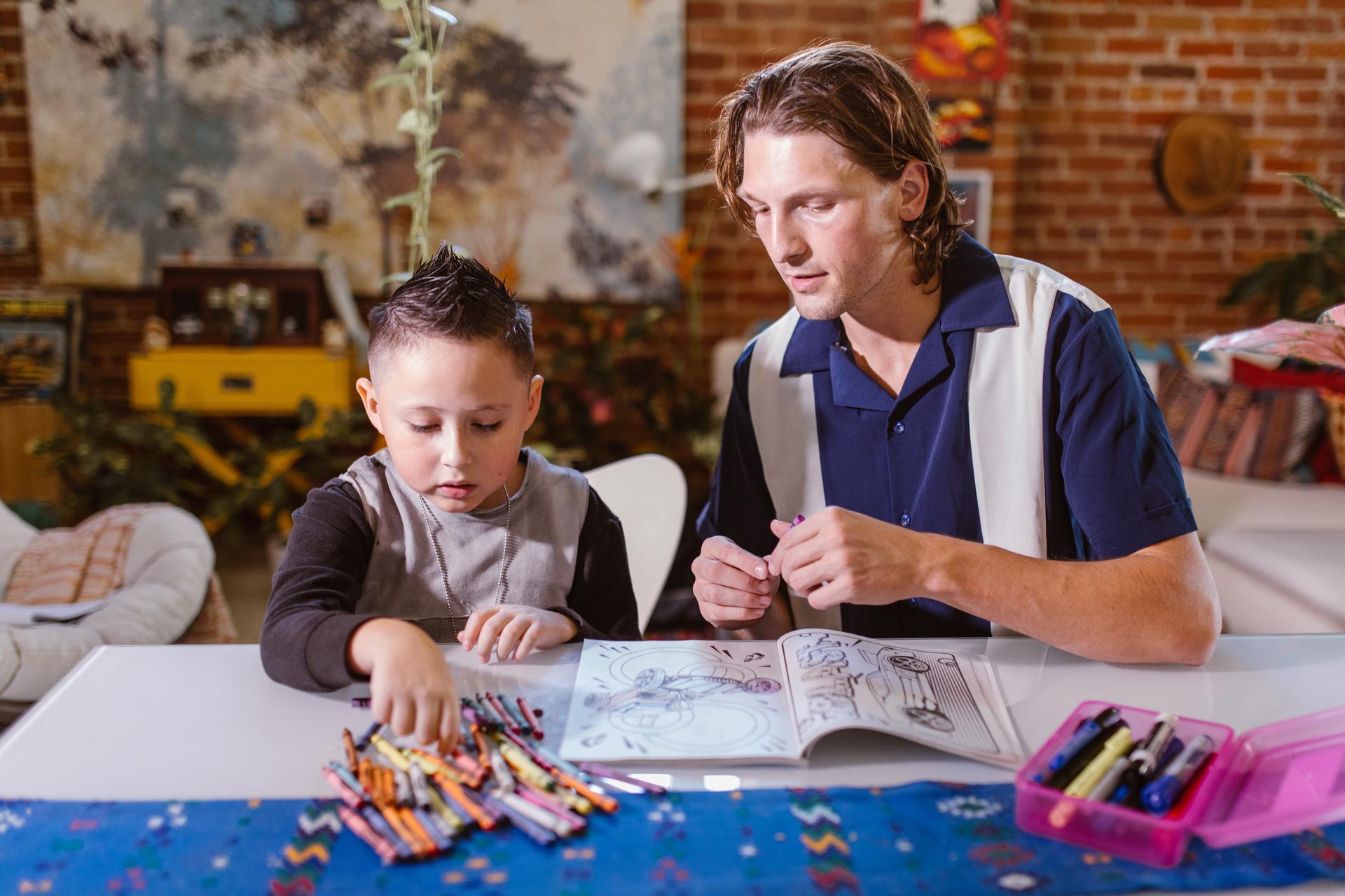 Young man and a small boy at a table with a coloring book and crayons