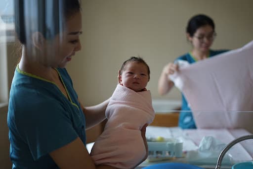 Nurse in scrubs cradling a swaddled newborn while a colleague prepares a blanket