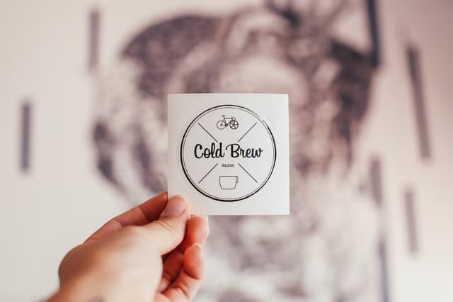 Crop person showing sticker of cafe with inscription