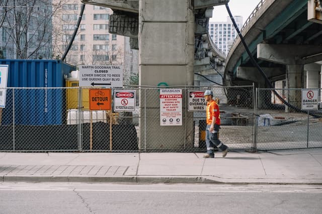 Worker in a hard hat walking past a fenced construction site, from the maintenance planner guide