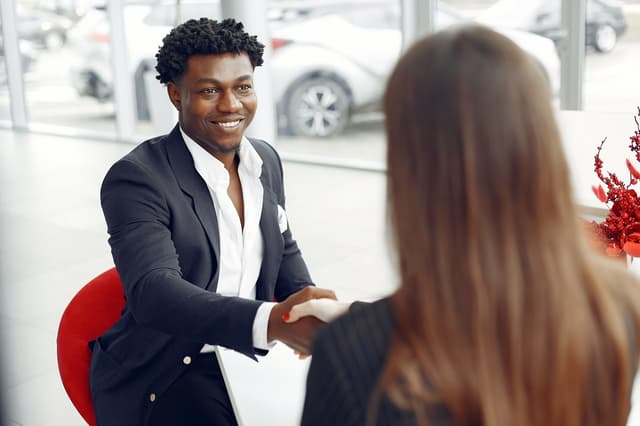 Man in a dark blazer smiling and shaking hands with a seated woman