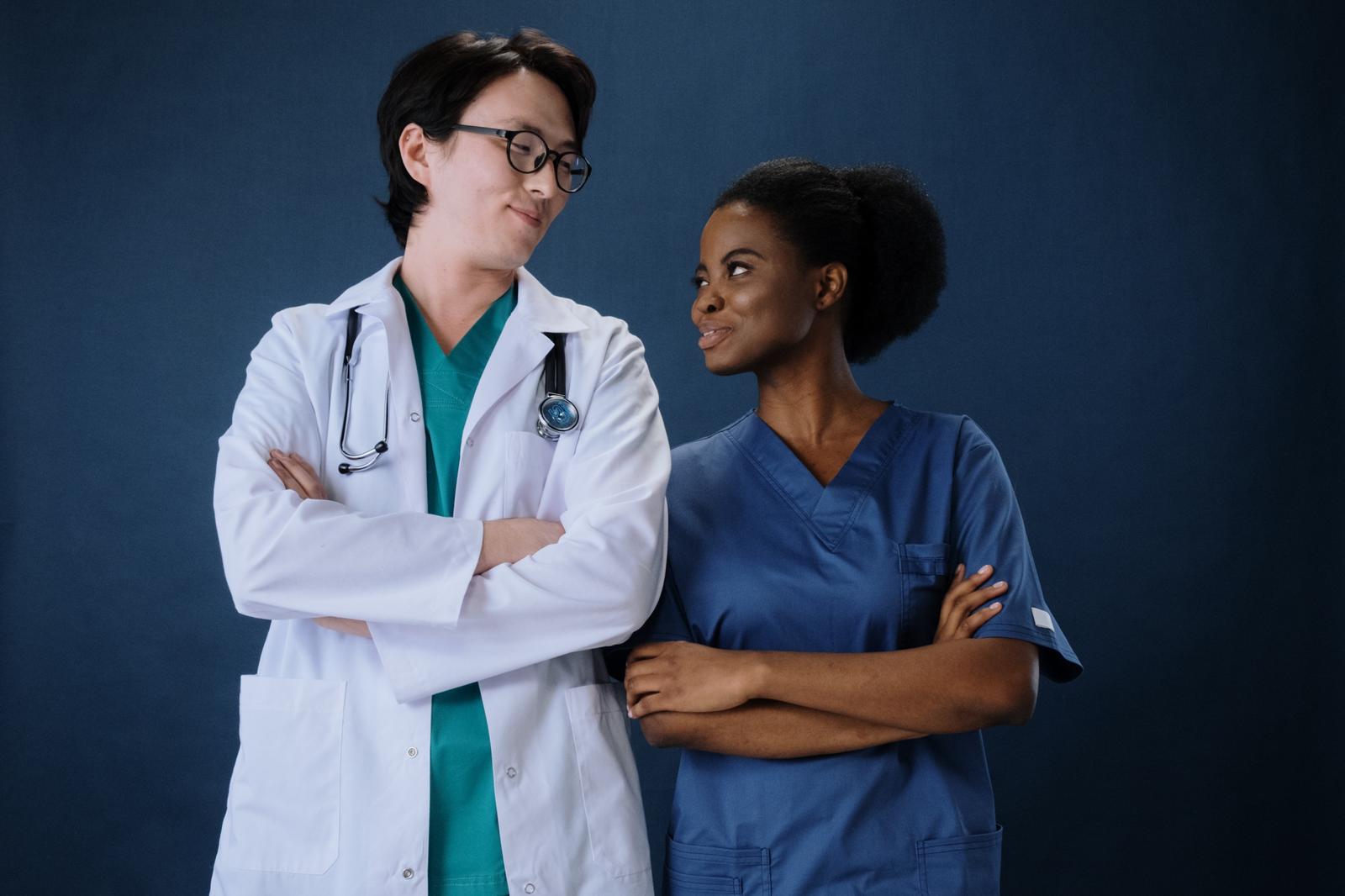 Doctor and nurse glancing at each other with folded arms against navy backdrop