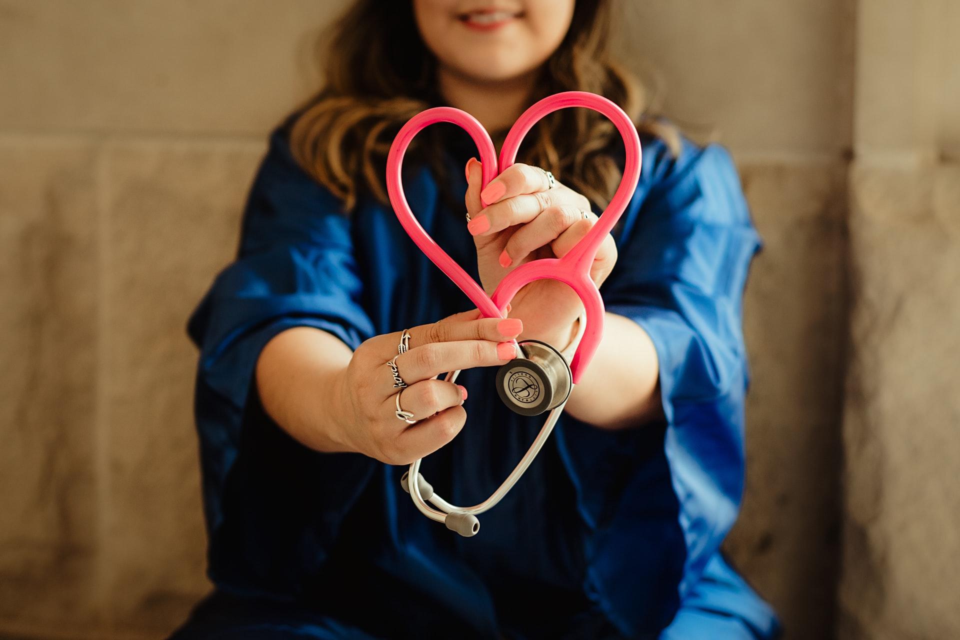 Nurse in scrubs holding a pink stethoscope in a heart shape, from the nursing interview guide