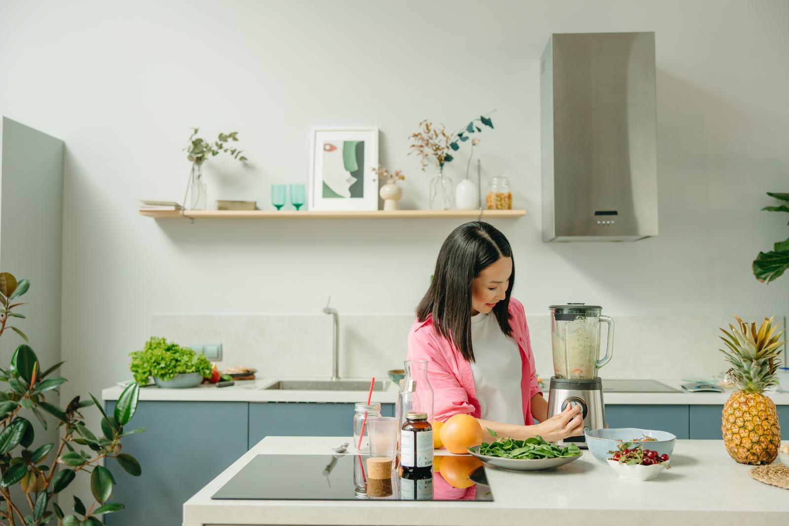 Woman preparing greens and a smoothie in a bright kitchen, from the nutritionist guide