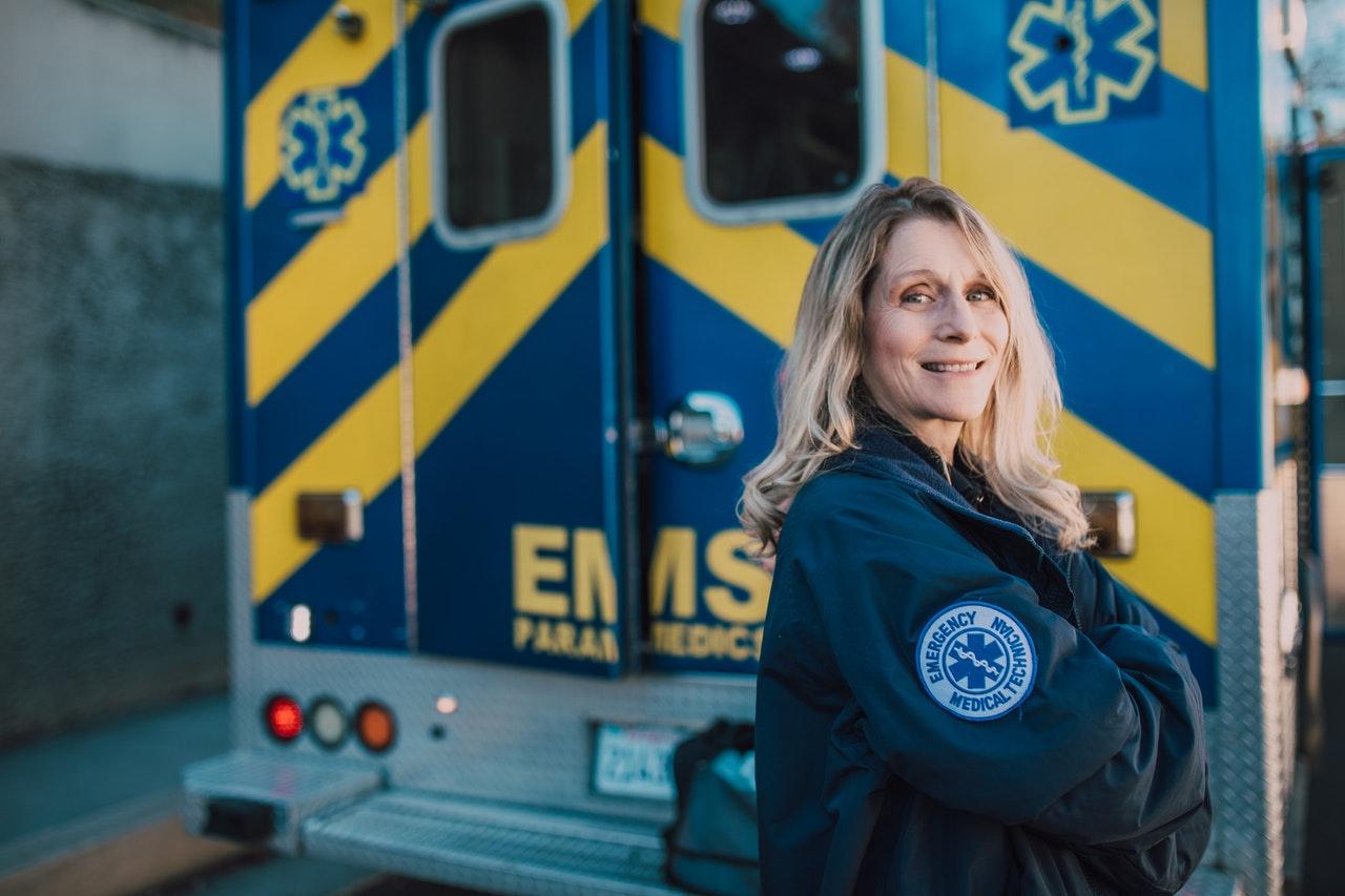 Smiling paramedic in an EMS jacket standing beside an ambulance's rear doors