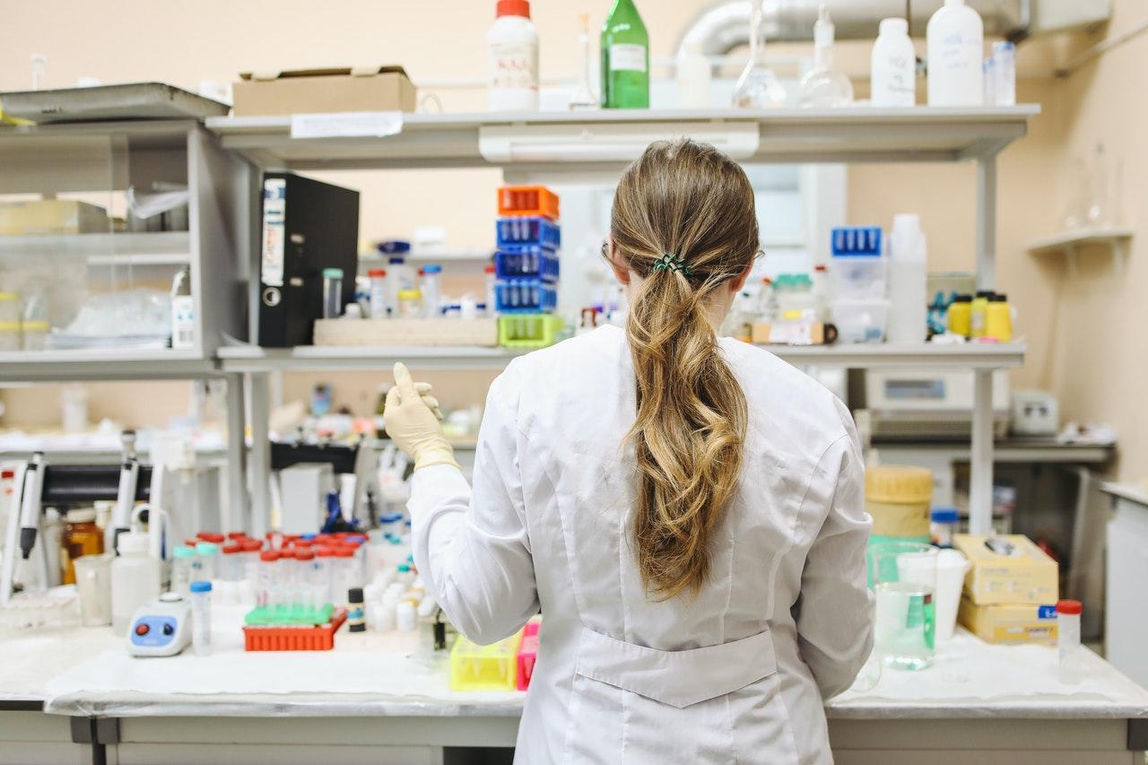 Person in a white lab coat working at a laboratory bench, viewed from behind