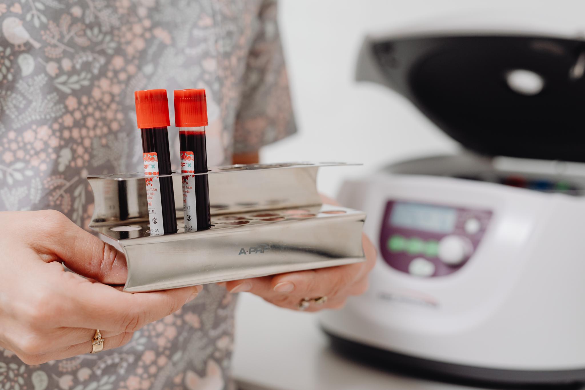 Technician holding a rack of blood sample tubes beside a centrifuge, from our phlebotomist career guide