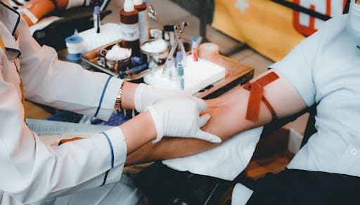 Gloved phlebotomist drawing blood from a patient's arm with tourniquet and collection tubes