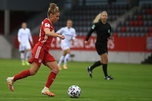 Soccer player in a red kit strikes the ball as the referee follows play