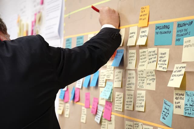 Man in a suit adding a sticky note to a crowded planning wall