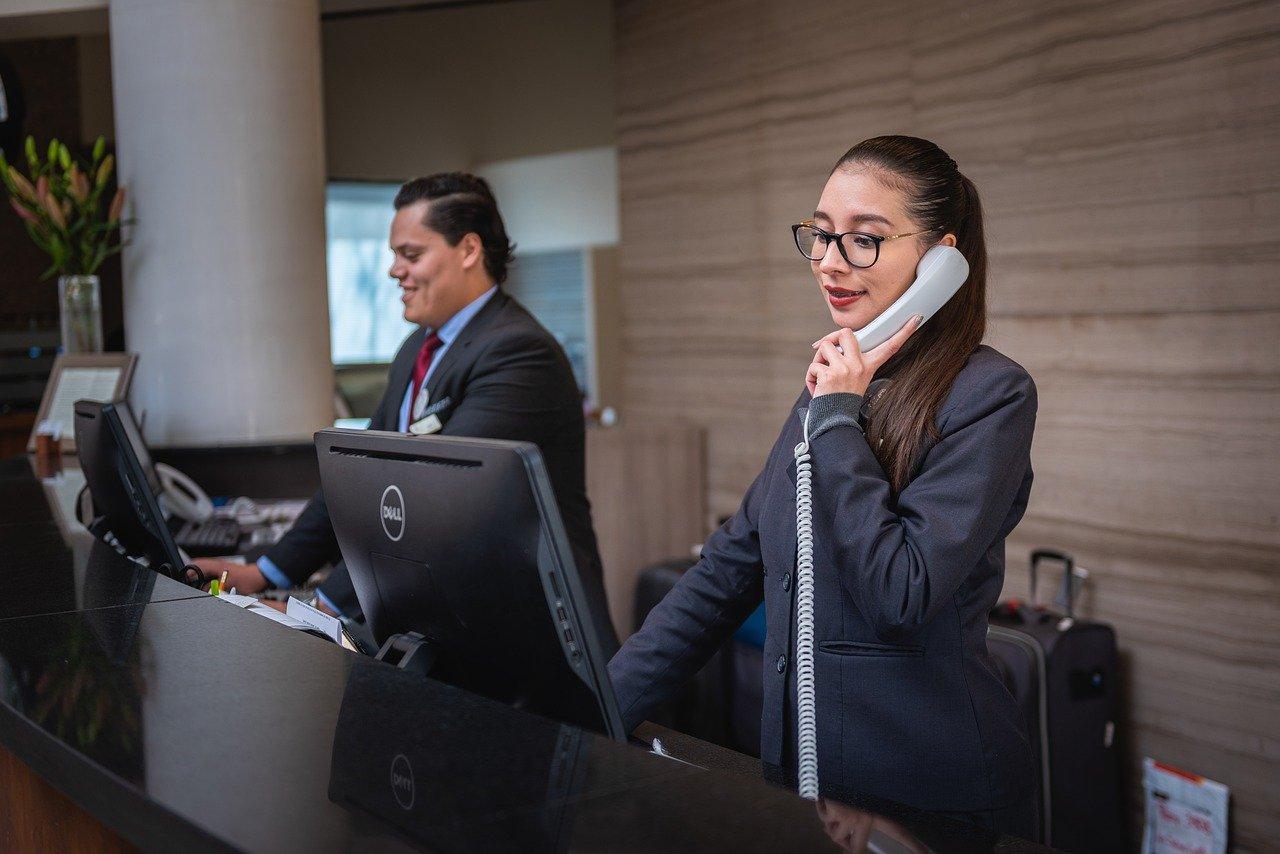 Hotel receptionist answering a desk phone while a colleague works at the front counter