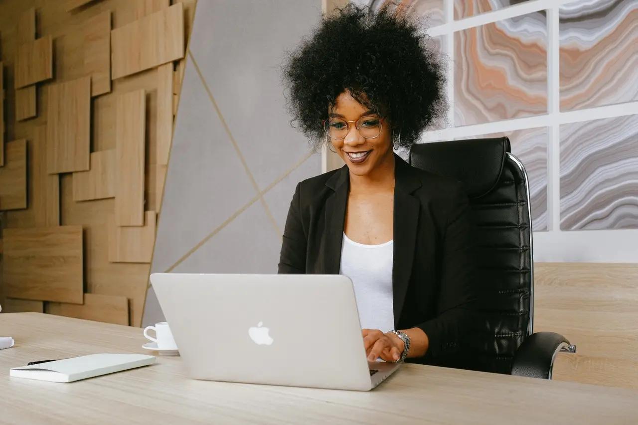 Smiling woman in a blazer typing on a laptop at an office desk