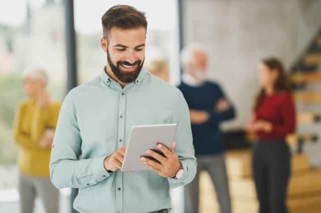 Smiling bearded man reading a tablet in an office, from the resume dos and don'ts guide