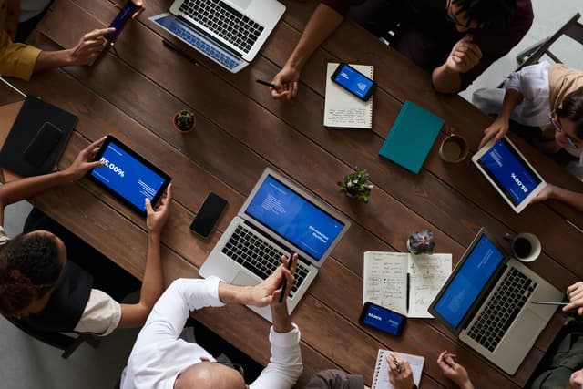 Overhead view of a team meeting with laptops, tablets and notes on a wooden table
