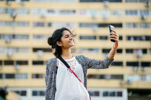 Young woman taking a phone selfie in front of a tall apartment block