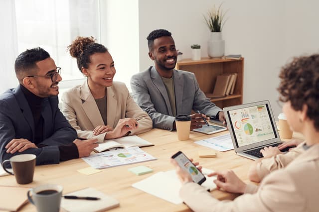 Colleagues smiling around a meeting table with a laptop showing colorful charts