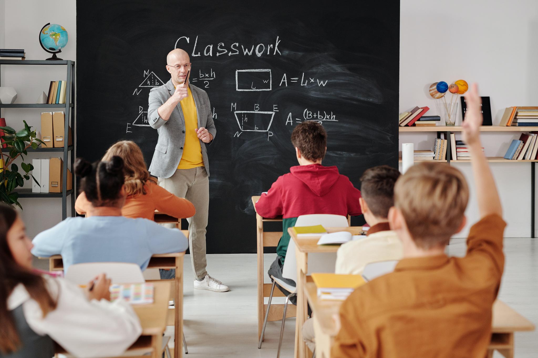Teacher at a blackboard of area formulas as a seated student raises a hand