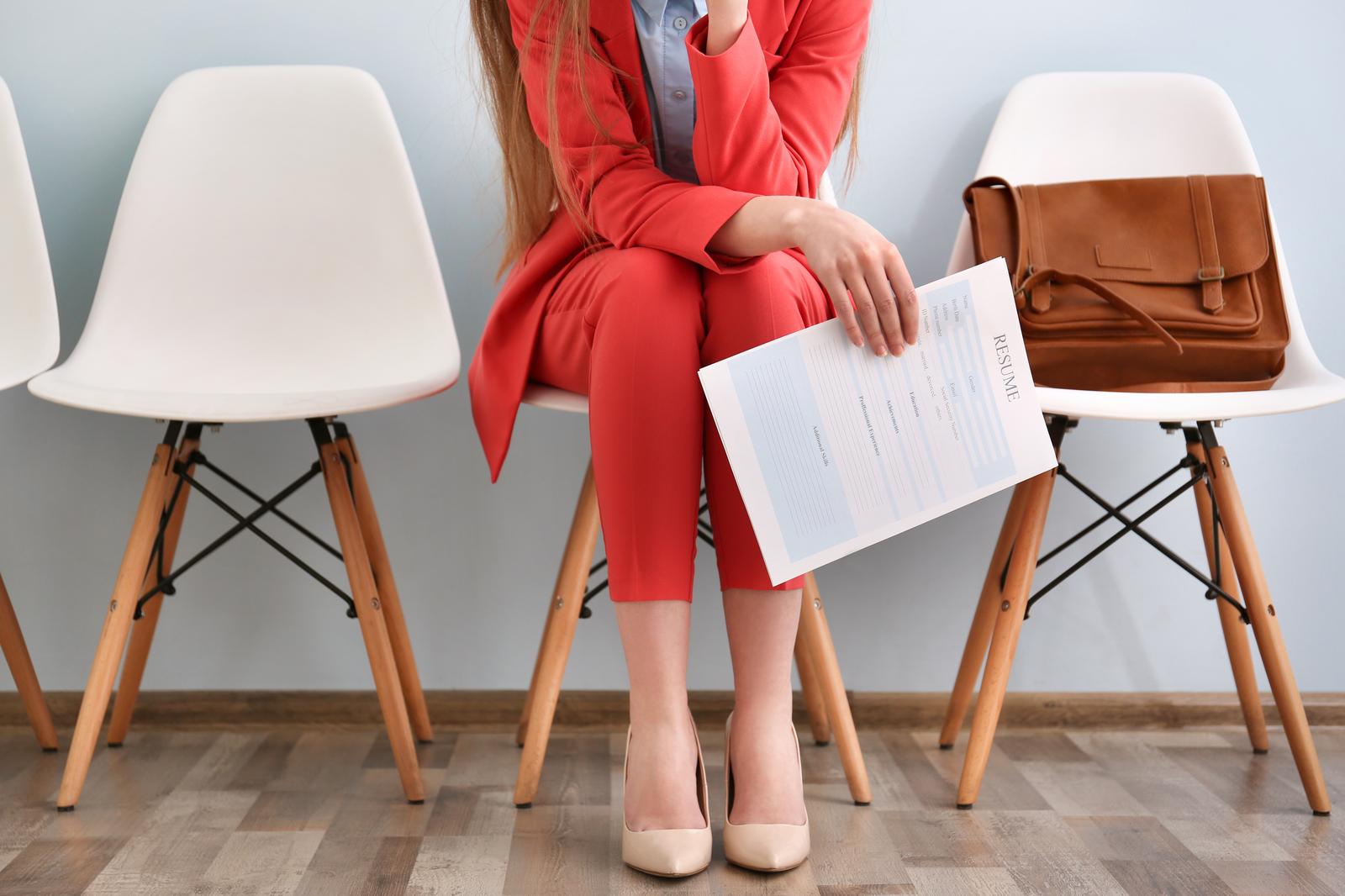 Woman in a red trouser suit holding a printed resume on a white chair