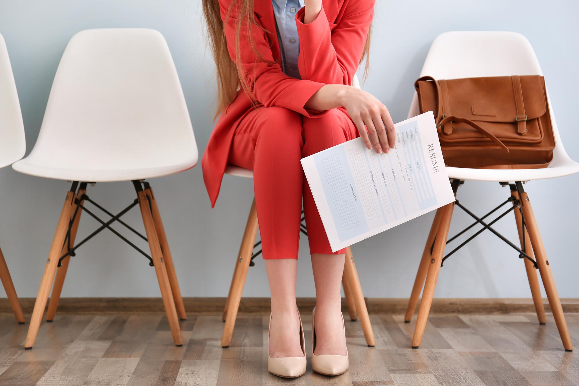 Woman in a red trouser suit holding a printed resume on a white chair