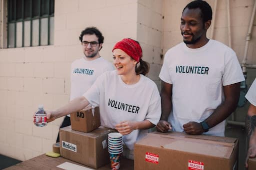 Three volunteers in matching shirts handing out water beside boxes marked aid and medicine