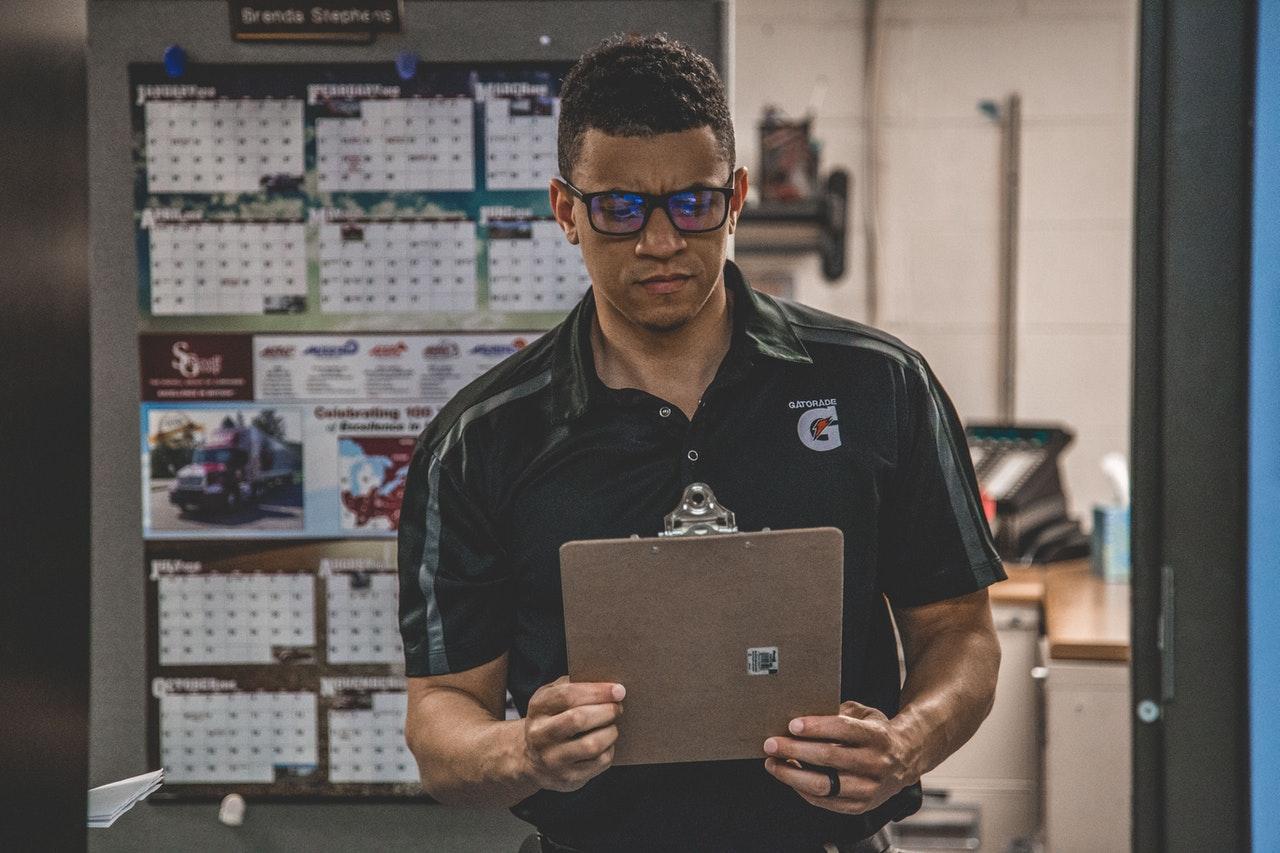 Man in a dark work polo reading a clipboard beside pinned wall calendars